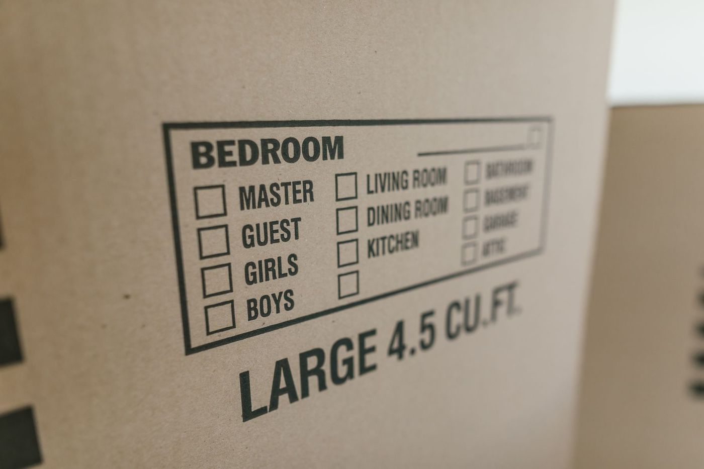 A large cardboard moving box printed with a room checklist — bedroom, living room, kitchen, garage — ready to be ticked